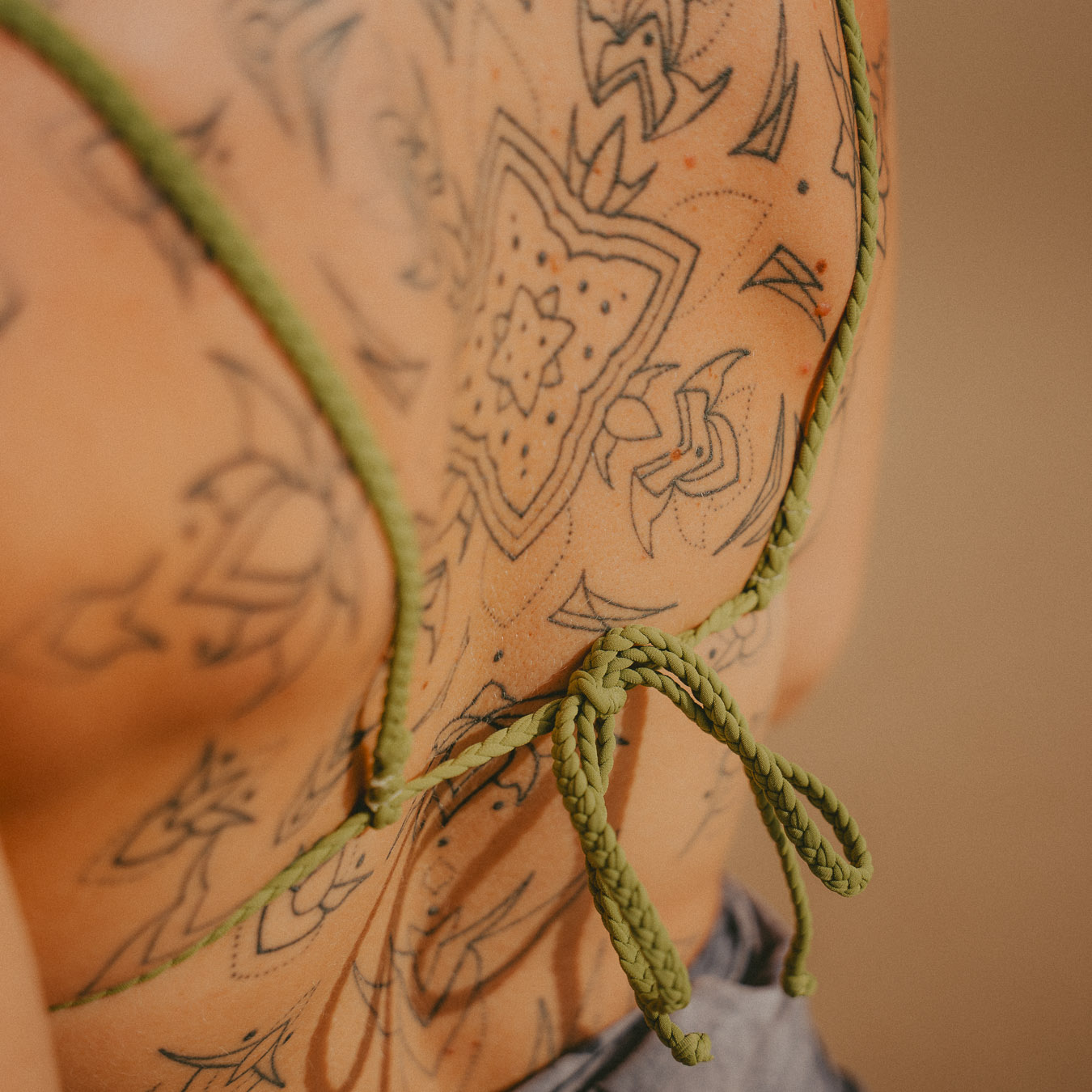 Close-up of braided green back tie on Cocou Conscious Couture bikini with intricate tattoo art on the model’s back