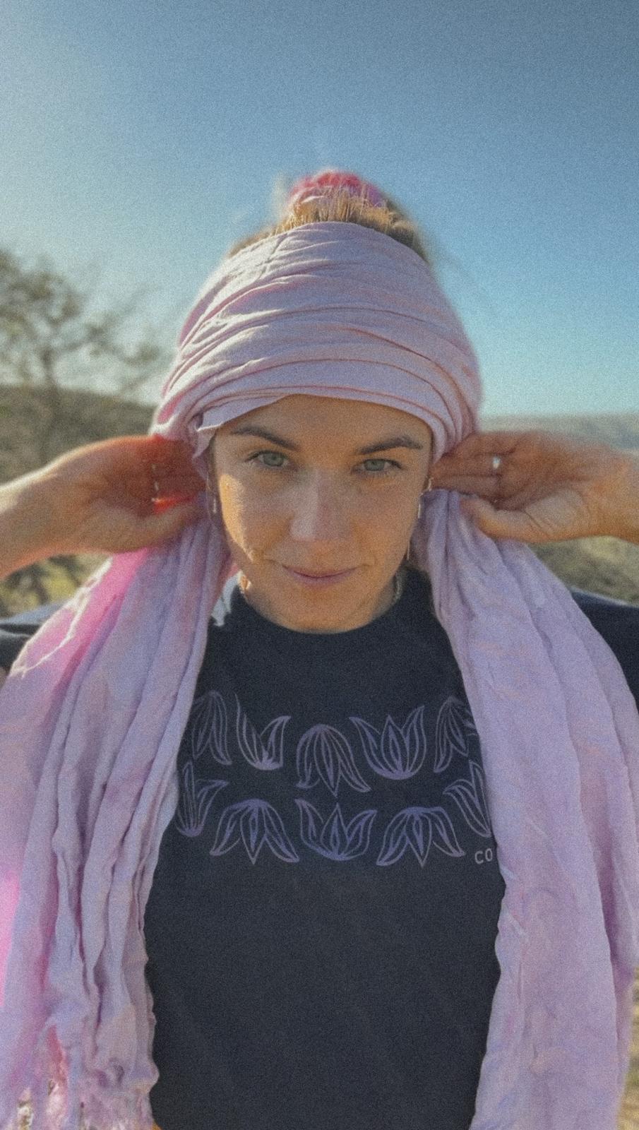 Woman wearing a dark blue shirt with lotus print, wrapping a lilac scarf around her head on a sunny day.
