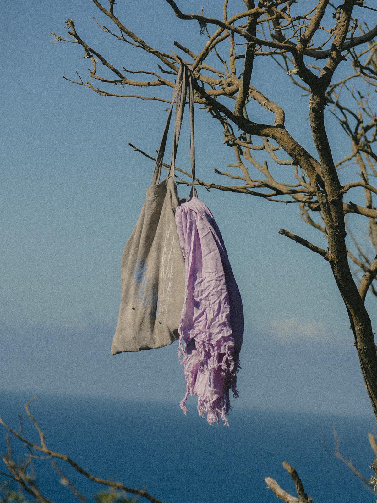 Sustainable cotton tote bag and lilac sarong hanging on a tree with the ocean in the background. Hand dyed Jute bag Forestwater