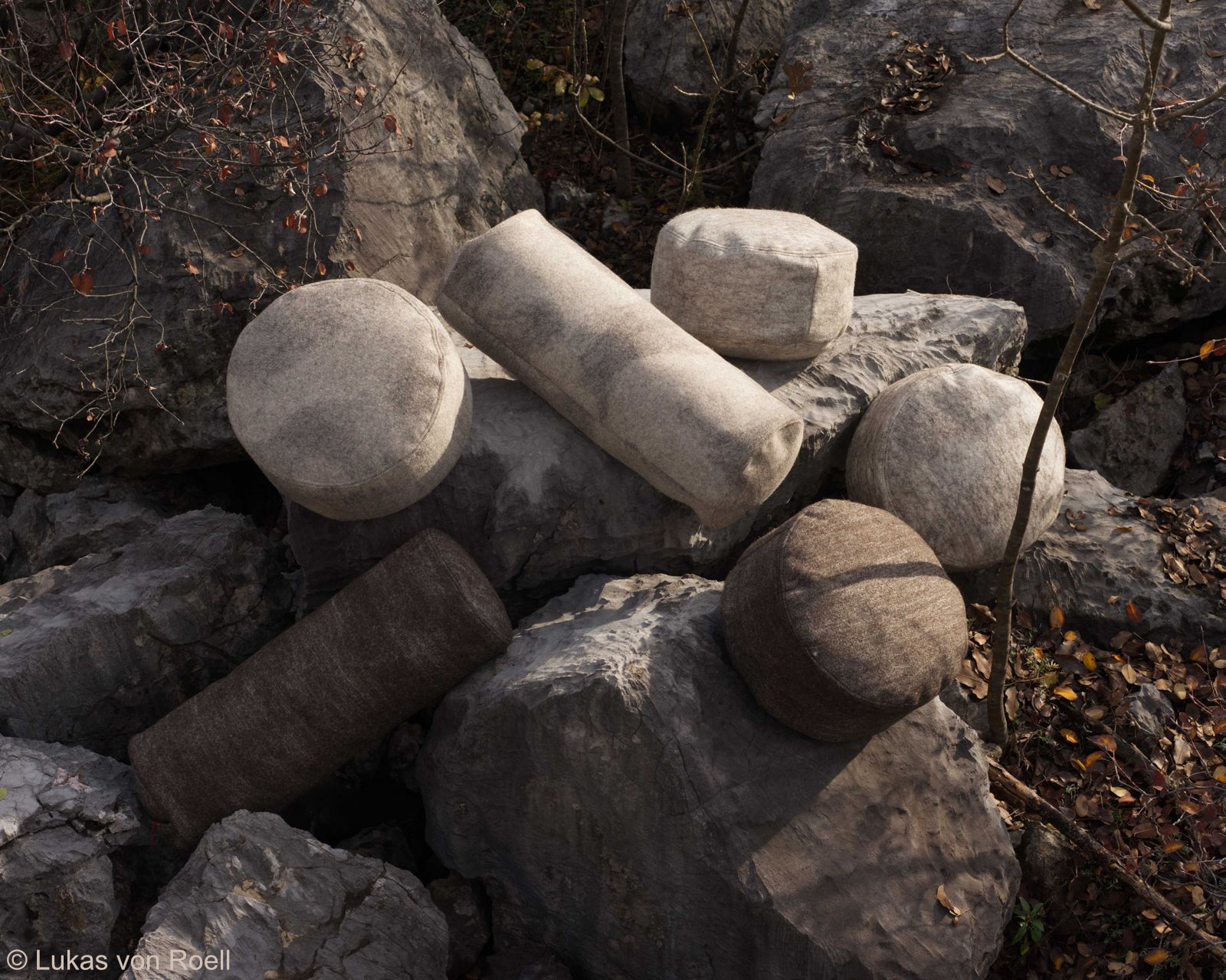 A collection of hand-felted wool meditation cushions and small seats, displayed on rugged rocks in natural light.