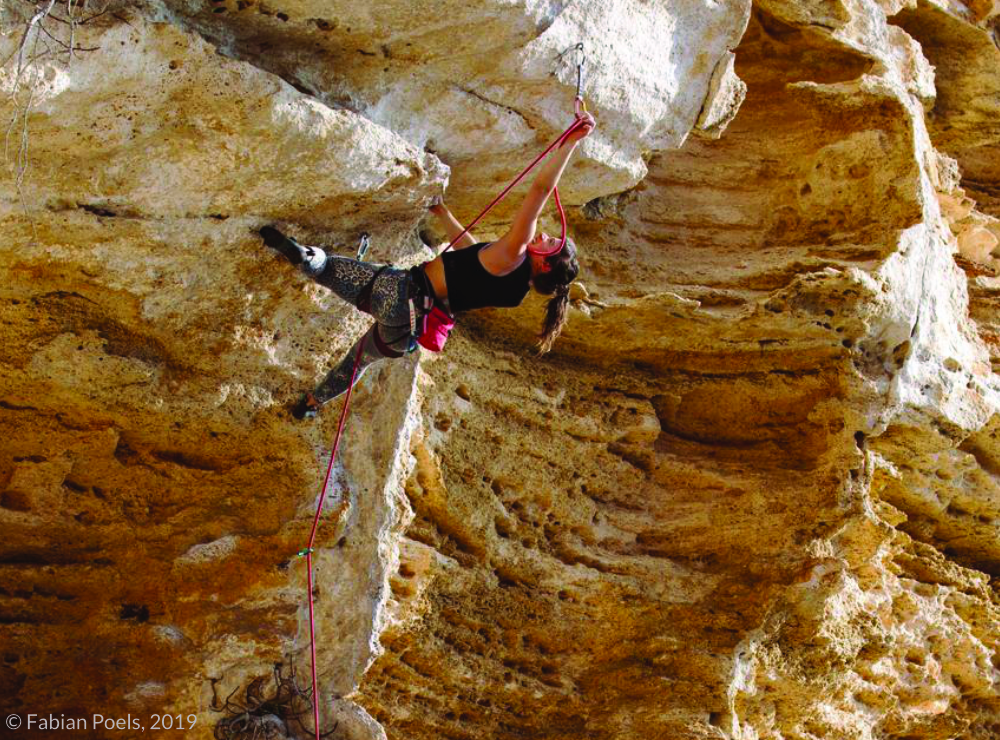 Theresa climbing a limestone cliff, wearing patterned leggings and a black tank top, emphasizing her adventurous and artistic spirit.