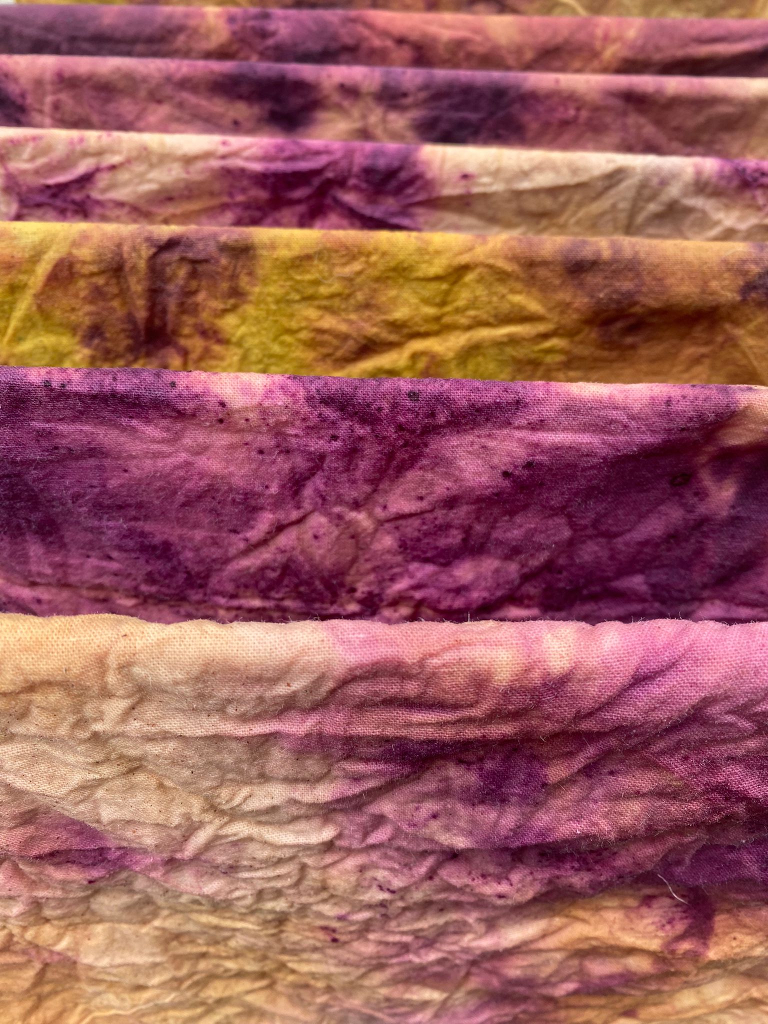 Close-up of hand-dyed organic fabric with deep purple and golden hues, showcasing the unique patterns created using natural dyes.