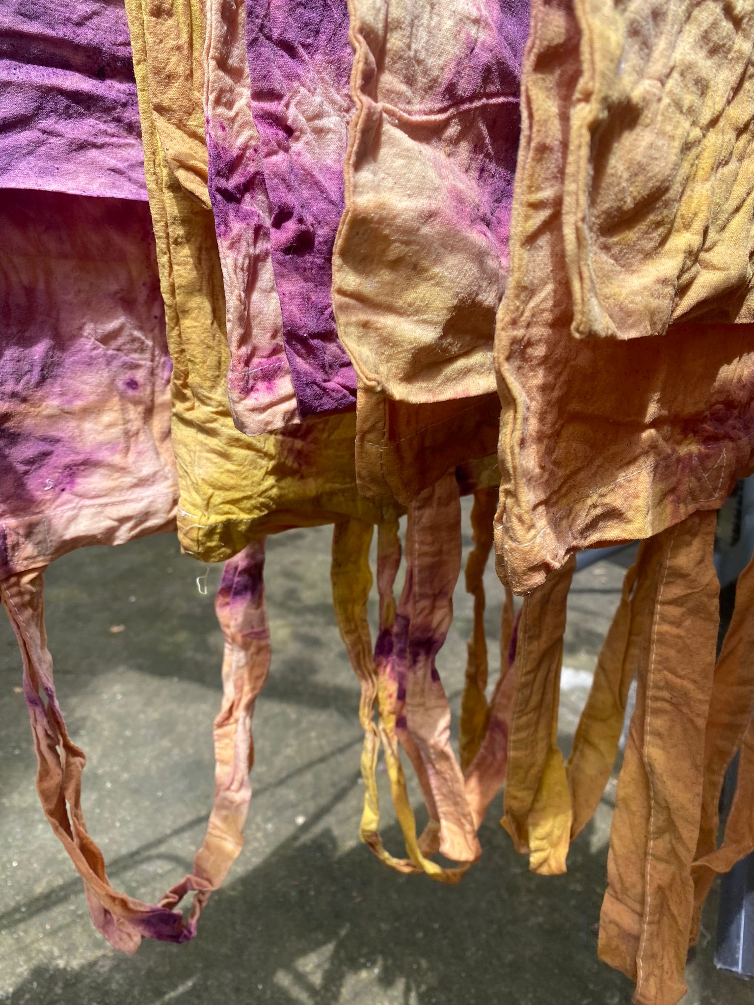 Hand-dyed organic fabric in warm hues of purple, yellow, and ochre, drying in the sun, representing sustainable and ethical craftsmanship.
