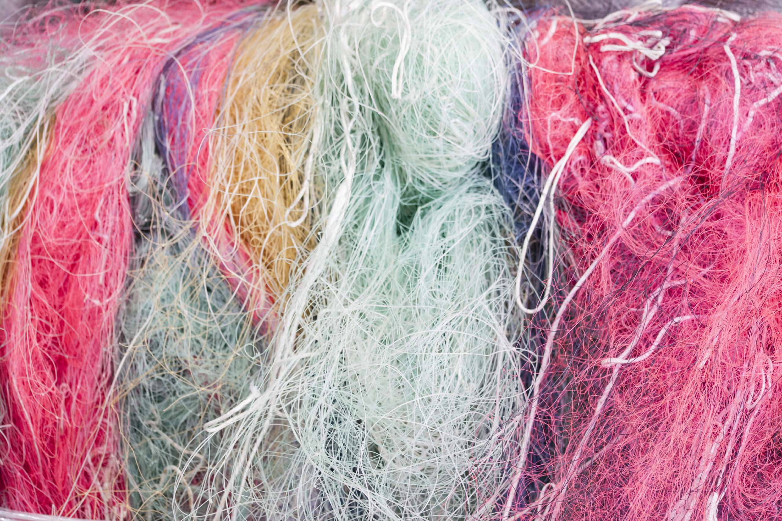 Recycled fishing nets in bright pink, green, and beige colors, prepared for transformation into ECONYL® regenerated nylon.